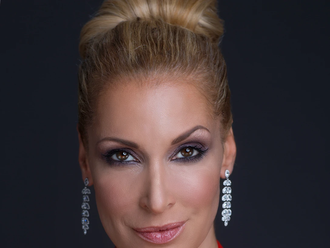 Tatiana Perez Porträt einer eleganten Frau mit blonden Haaren und rotem Kleid vor dunklem Hintergrund.</p>Portrait of an elegant woman with blonde hair and a red dress against a dark background.</p> <p