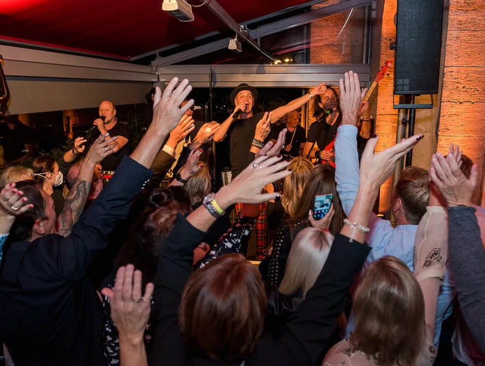Brings Geb Menschenmenge jubelt einer auf der Bühne singenden Band in einem stimmungsvoll beleuchteten Raum zu.</p>Crowd cheers a band singing on stage in an atmospherically lit room.</p> <p