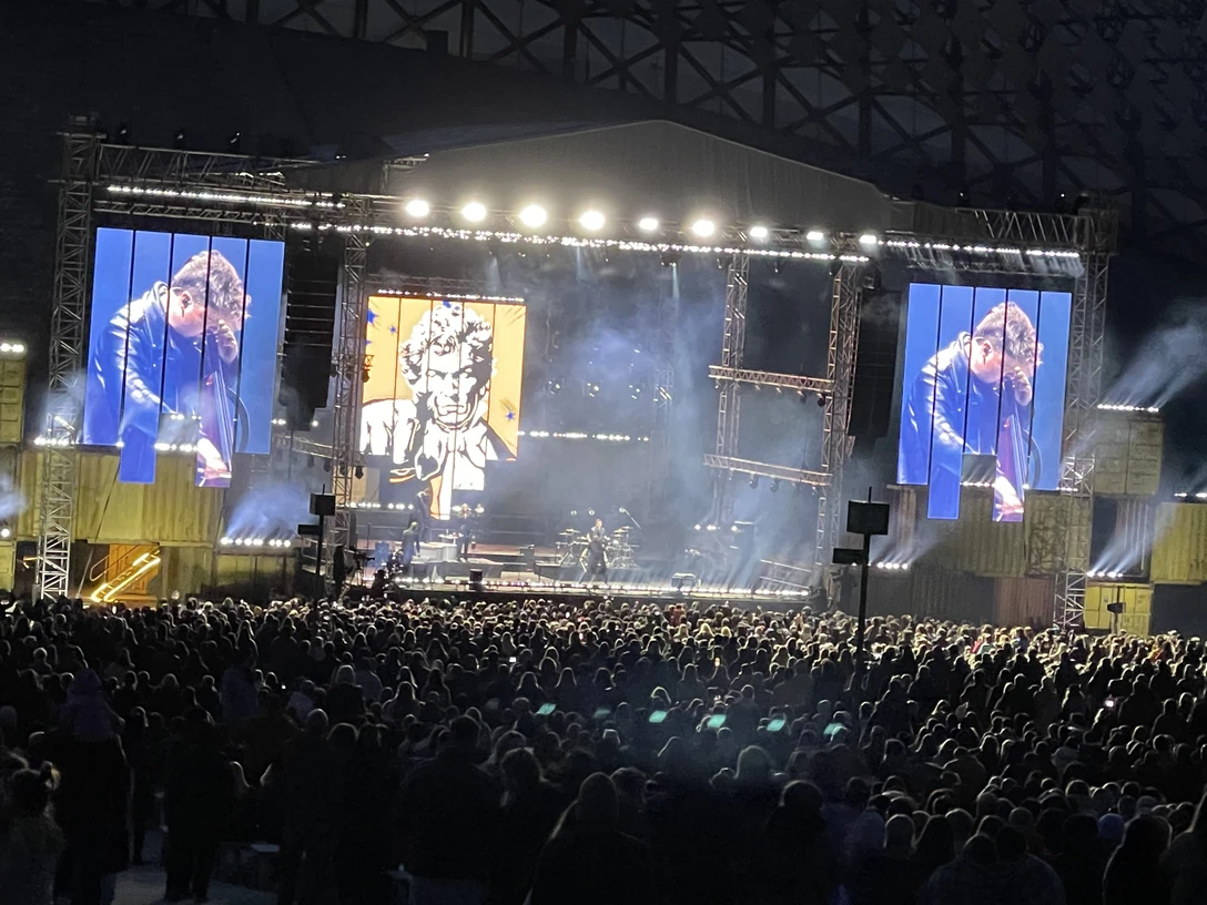 Dagamba Open-Air-Konzert bei Nacht mit beleuchteter Bühne, großer Menschenmenge und Videobildschirm.</p>Open-air concert at night with illuminated stage, large crowd and video screen.</p> <p