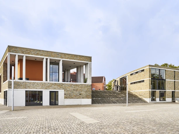 Kulturzentrum_Aussen_047.jpg Modernes Gebäude mit Glasfronten und Backsteinmauern auf einem gepflasterten Platz bei klarem Himmel.</p>