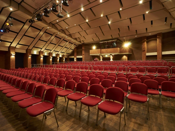 Kulturzentrum_grosser_Saal_083.jpg Ein leerer Konzertsaal mit roten Stühlen und beleuchtetem Holzboden unter einer gewölbten Decke.</p>