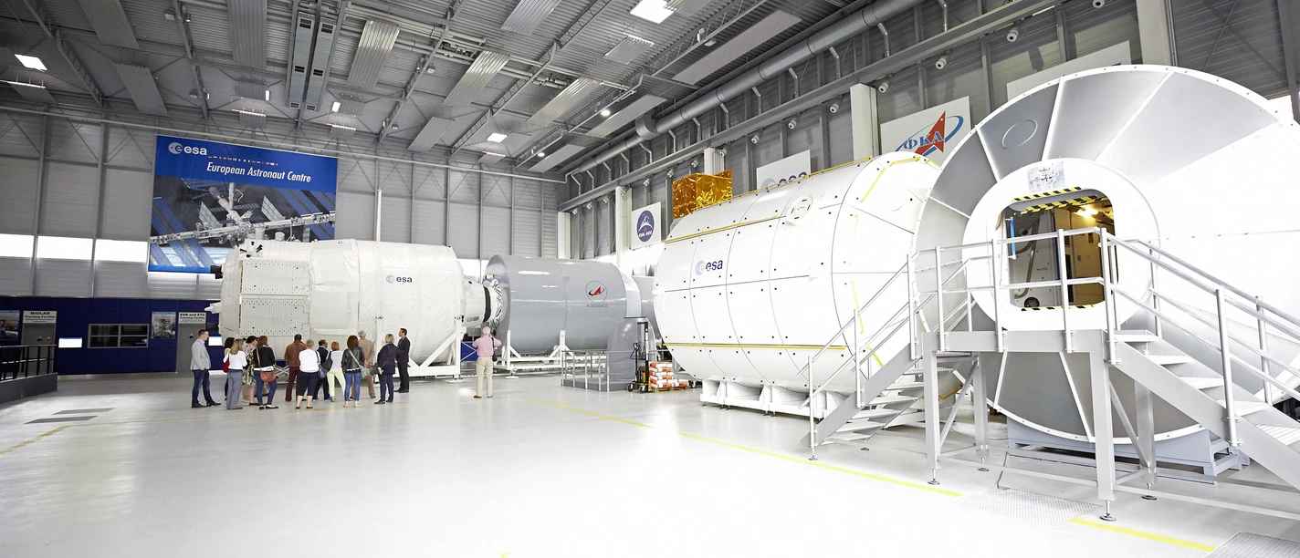 Europäisches Astronautenzentrum Mockup von Raumfahrtmodulen in einem modernen, großen Hochtechnologielabor mit Besuchern und ESA-Logo.