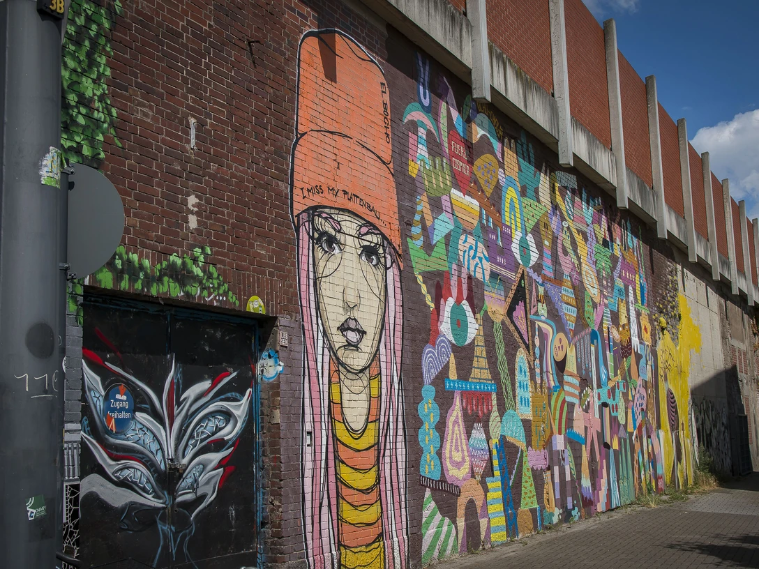 Street Art in Köln Ehrenfeld <p>Buntes Graffiti-Kunstwerk auf roter Backsteinwand zeigt Porträt und abstrakte Formen in leuchtenden Farben.</p><p>Colorful graffiti artwork on red brick wall shows portrait and abstract shapes in bright colors.</p>