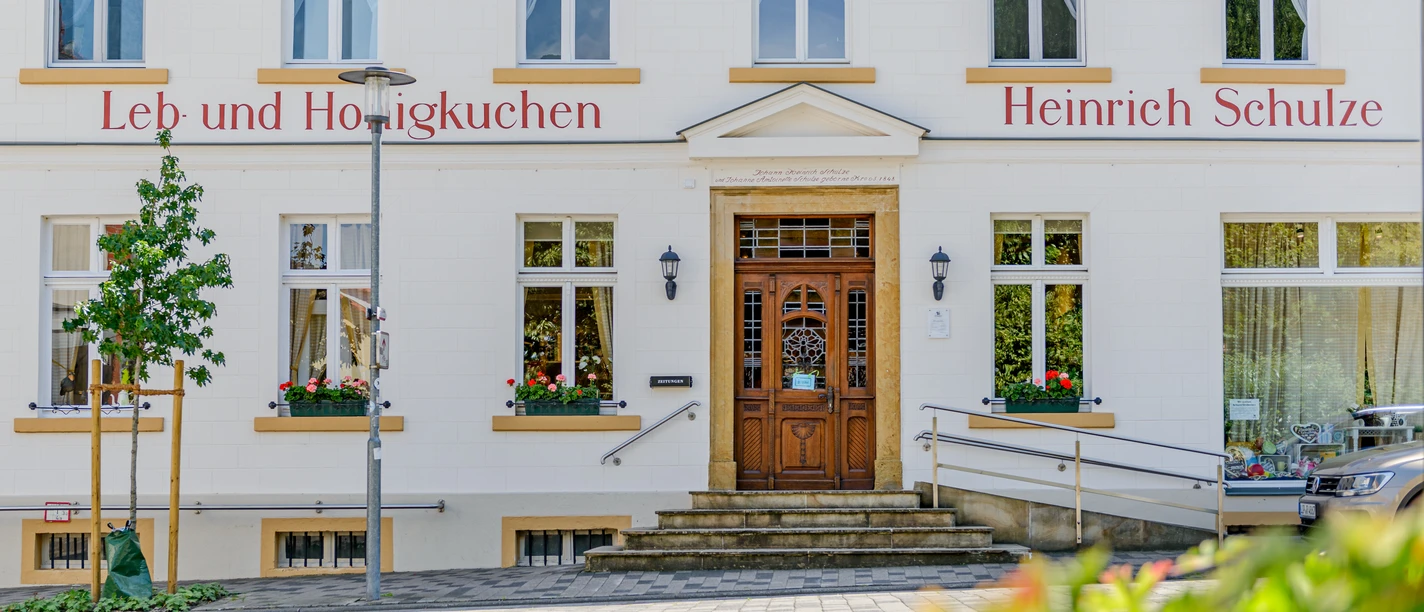 Das Bild zeigt die Fassade einer traditionellen Lebkuchen-Bäckerei mit Stufen und Blumendekoration.