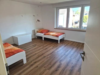 Zweibettzimmer mit Holzboden, zwei Einzelbetten und großem Fenster, hell und funktional gestaltet.