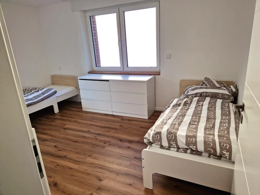 Zweibettzimmer mit Holzfußboden, zwei Einzelbetten, Kommode und Fenster mit Tageslicht.