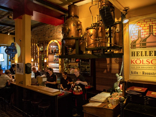 hellers-brauhaus-005.JPG Eine gemütliche Brauhaus-Szene zeigt Menschen an einer Bar, umgeben von Brauereiausrüstung.