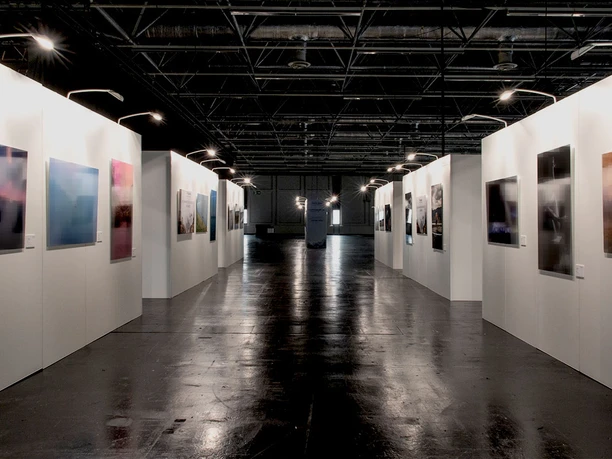 Galerie mit beleuchteten modernen Kunstwerken an weißen Wänden, schwarzer Hochglanzfußboden.