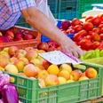 Wochenmarkt (1).png Frischwarenstand auf einem Markt zeigt bunte Früchte wie Äpfel, Tomaten und Paprika in Kisten.