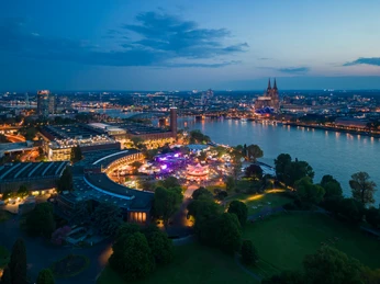 Tanzbrunnen Köln, Drohnenaufnahme bei Nacht Blick auf das beleuchtete Köln bei Nacht mit Dom und Rhein. Ein Riesenrad erstrahlt im Vordergrund.</p>View of illuminated Cologne at night with the cathedral and the Rhine. A Ferris wheel shines in the foreground.</p>