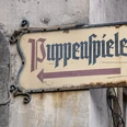Hänneschen Theater Schild mit "Puppenspiele", an einer Gebäudewand angebracht.Sign with "Puppenspiele", attached to a building wall.