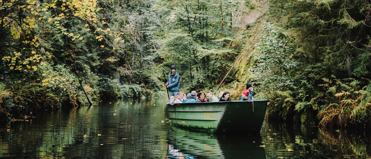 Wild gorge A group of people are sitting in a green boat sailing through a wooded river; the atmosphere is calm and close to nature.