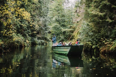 Wilde Klamm Eine Gruppe von Menschen sitzt in einem grünen Boot, das durch einen bewaldeten Fluss fährt; die Atmosphäre ist ruhig und naturverbunden.