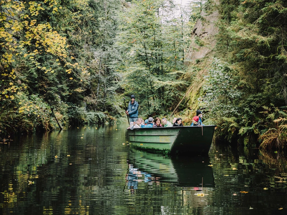 Wilde Klamm Eine Gruppe von Menschen sitzt in einem grünen Boot, das durch einen bewaldeten Fluss fährt; die Atmosphäre ist ruhig und naturverbunden.