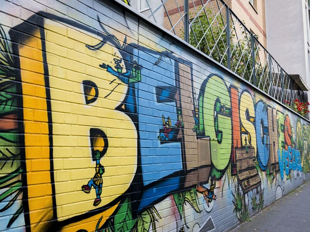 Street Art im Belgischen Viertel Auf einer langen, farbenfrohen Mauer sind große Graffiti-Buchstaben zusehen, die verspielte Details zeigen.