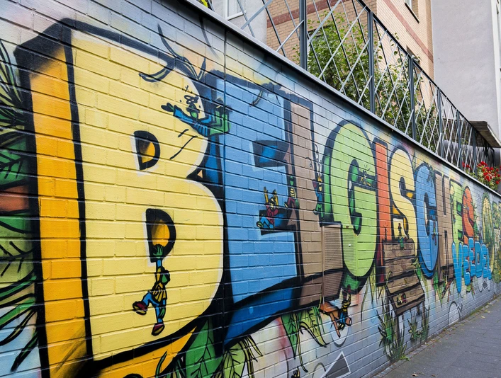 Street Art im Belgischen Viertel Auf einer langen, farbenfrohen Mauer sind große Graffiti-Buchstaben zusehen, die verspielte Details zeigen.