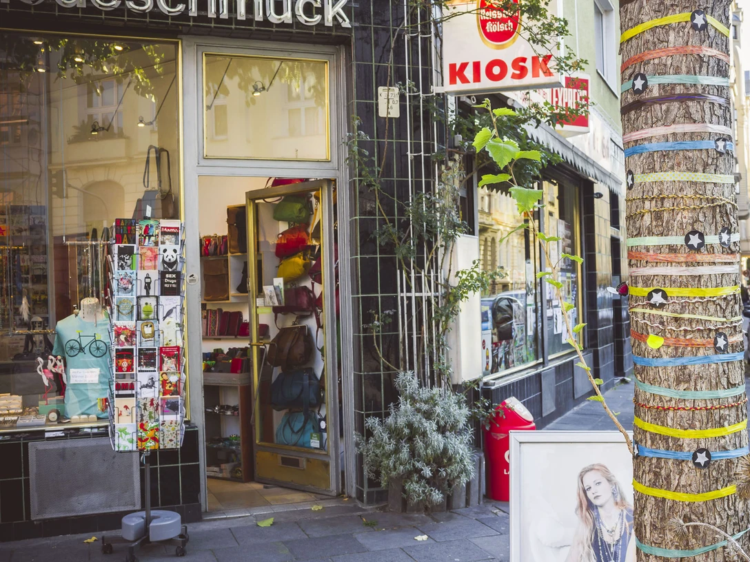 Belgian Quarter in Cologne Ein traditioneller Kiosk in Köln bietet farbenfrohe Waren aller Art. Ein Baum vor dem Laden ist mit bunten Bändern und Sternen dekoriert, was der Straße ein lebendiges Flair verleiht.A traditional kiosk in Cologne offers colorful goods of all kinds. A tree in front of the store is decorated with colorful ribbons and stars, giving the street a lively flair.