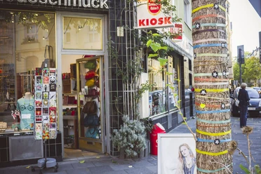 Belgisches Viertel in Köln Ein traditioneller Kiosk in Köln bietet farbenfrohe Waren aller Art. Ein Baum vor dem Laden ist mit bunten Bändern und Sternen dekoriert, was der Straße ein lebendiges Flair verleiht.