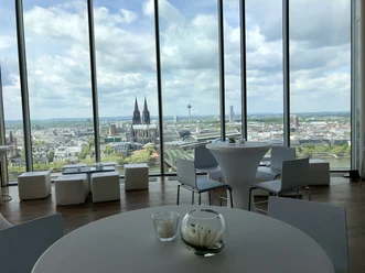 Firmenfeier_KölnSKY Blick aus Panoramafenster auf die Kölner Skyline mit Dom, Fluss und Wolkenhimmel.</p>