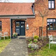 Cafe_EneHus03_032024_PetraRoemer.jpg Rotes Ziegelhaus mit Gehweg davor und Sitzecken links und rechts
