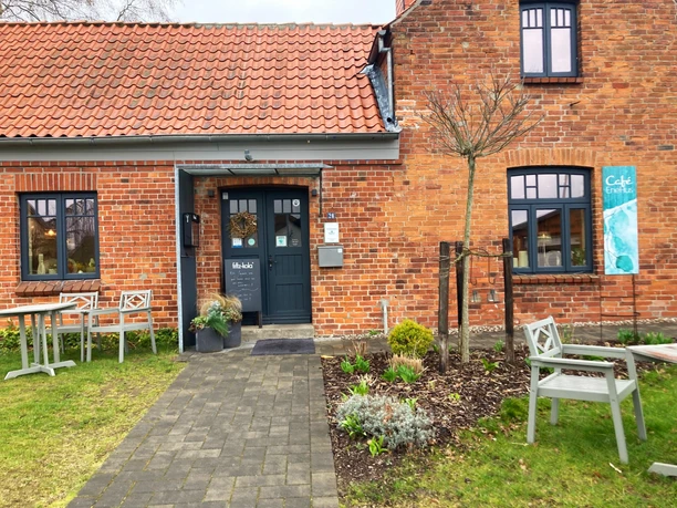 Cafe_EneHus03_032024_PetraRoemer.jpg Rotes Ziegelhaus mit Gehweg davor und Sitzecken links und rechts