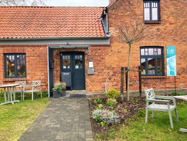 Cafe_EneHus03_032024_PetraRoemer.jpg Rotes Ziegelhaus mit Gehweg davor und Sitzecken links und rechts