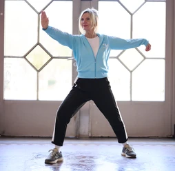 Qigong Cordula_Theine.jpg Frau in blauer Trainingsjacke und schwarzer Hose praktiziert eine dynamische Qigong-Übung.
