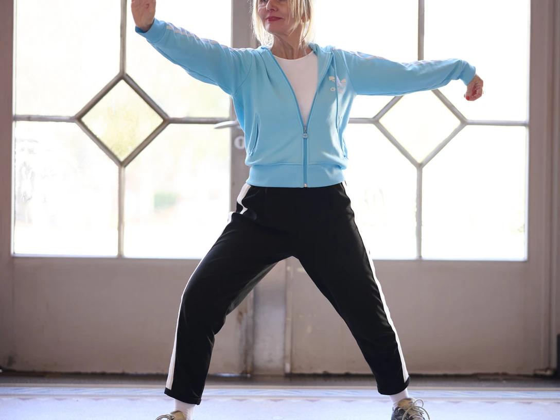 Qigong Cordula_Theine.jpg Frau in blauer Trainingsjacke und schwarzer Hose praktiziert eine dynamische Qigong-Übung.