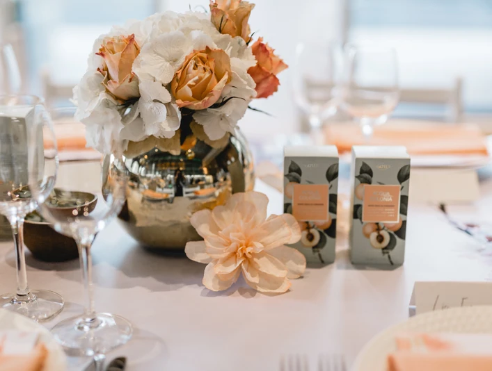 4711 Duftmenü Blumenvase mit Rosen und weißen Blumen auf einem elegant gedeckten Tisch, umgeben von Weingläsern.Flower vase with roses and white flowers on an elegantly laid table, surrounded by wine glasses.