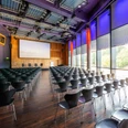 KOMED-Saal Moderner Konferenzraum mit dunklen Stühlen, großem Bildschirm und lila beleuchteten Wänden.</p>Modern conference room with dark chairs, large screen and purple-lit walls.</p> <p