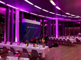 KölnSKY_Dinner_Firmenevent Eleganter, in pinkes Licht getauchter Veranstaltungsraum mit gedeckten Tischen und Bühne.</p>