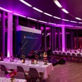 KölnSKY_Dinner_Firmenevent Eleganter, in pinkes Licht getauchter Veranstaltungsraum mit gedeckten Tischen und Bühne.</p>Elegant event room bathed in pink light with set tables and stage.</p> <p