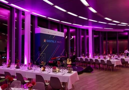 KölnSKY_Dinner_Firmenevent Eleganter, in pinkes Licht getauchter Veranstaltungsraum mit gedeckten Tischen und Bühne.</p>Elegant event room bathed in pink light with set tables and stage.</p> <p