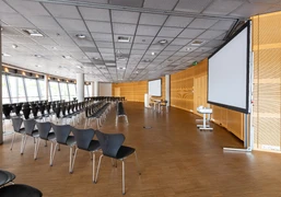 Raum 1-3 Ein moderner Konferenzraum mit leeren Stuhlreihen und zwei großen Bildschirmen.</p>A modern conference room with empty rows of chairs and two large screens.</p> <p