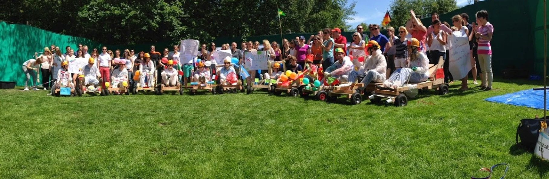 Teamevent.jpg Gruppenfoto beim Teamevent auf dem Rasen mit selbstgebastelten KartautosGroup photo at the team event on the lawn with self-made go-kart cars