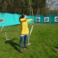 Bogenschießen.JPG Zwei junge Frauen stehen auf einer grünen Wiese und schießen mit dem Bogen auf Zielscheiben. Die Bögen sind gespannt und schussbereit.Two young women stand on a green meadow and shoot at targets with their bows. The bows are strung and ready to shoot.