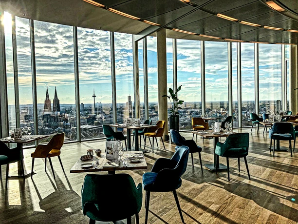 KölnSKY Brunch A modern restaurant with a panoramic view of a city, with chairs and set tables.