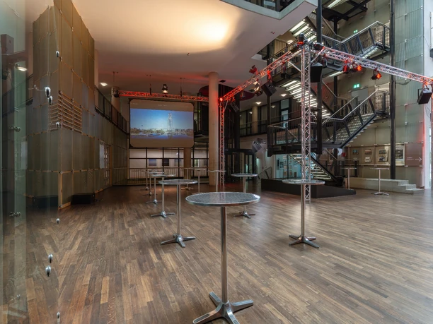 Saal-Foyer Offener Veranstaltungsraum mit Holzboden, Stehtischen und modernen Beleuchtungsanlagen.