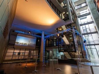 Saal-Foyer Moderner Innenraum mit Bühne, beleuchtet in Blau, und rollstuhlgerechten Zugängen.</p>Modern interior with stage, illuminated in blue, and wheelchair-accessible entrances.</p> <p