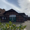 Bild 4.jpg Das Bild zeigt ein traditionelles Fachwerkgebäude mit der Aufschrift "Mühlen Café Ammerland". Der Vordergrund sind Pflanzen zu sehen, die dem Bild eine natürliche Note geben.