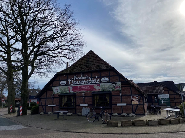 Bild 5.jpg Das Bild zeigt ein traditionelles Fachwerkgebäude mit der Aufschrift "Knuth's Bauernscheune". Fahrräder und eine Sitzbank vor dem Eingang sind erkennbar. Der Himmel ist leicht bewölkt.