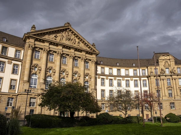 Oberlandesgericht Oberlandesgericht Köln im neoklassizistischen Stil, umgeben von gepflegtem Grün unter dramatischem Himmel.