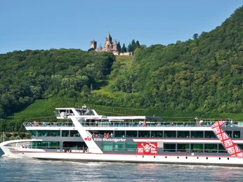 MS_RheinFantasie A white excursion boat sails in front of a wooded hill with a castle on the slope.</p> <p