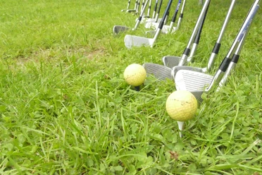 Crossgolf.jpg Golfschläger und Bälle auf grünem Rasen, bereit zum Abschlag.