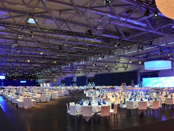 Abendveranstaltung Large, elegantly lit banquet hall with white-clothed tables and glamorous lighting effects.</p> <p