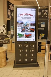 EDEKA Center Werle.jpg Digitale Infotafel mit Werbung und Ladeoptionen im Eingangsbereich eines Geschäfts.