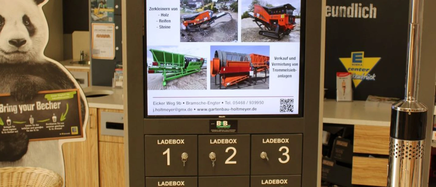 EDEKA Center Werle.jpg Digitale Infotafel mit Werbung und Ladeoptionen im Eingangsbereich eines Geschäfts.