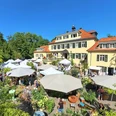 Rosenfest Ein idyllischer Gartenmarkt mit weißen Pavillons vor einem großen, eleganten Gebäude im Sonnenschein.
