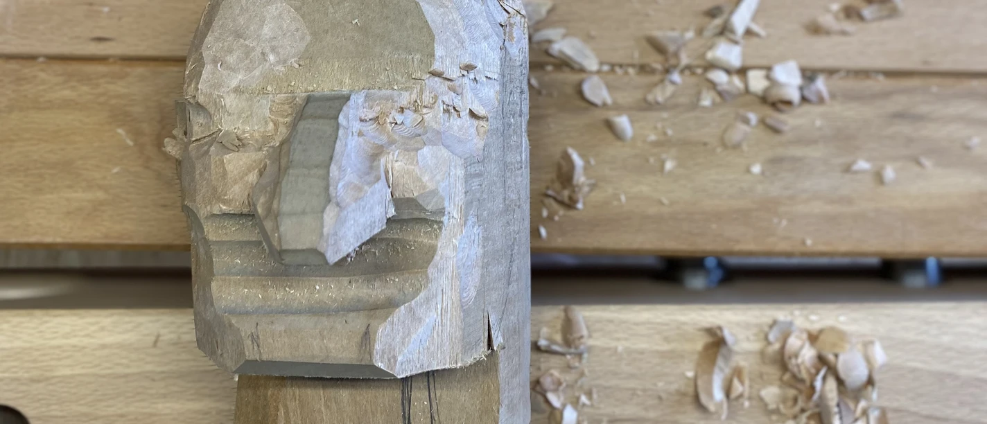 Kasper Schnitzkopf Holzskulptur eines Gesichts in Arbeit auf einer Werkbank, umgeben von Holzspänen.