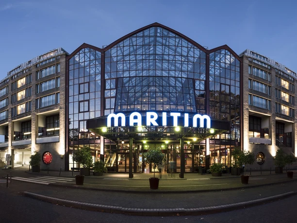 Maritim Hotel Köln Das Maritim Hotel mit Glasfassade und beleuchtetem Eingang in der Abenddämmerung.</p>
